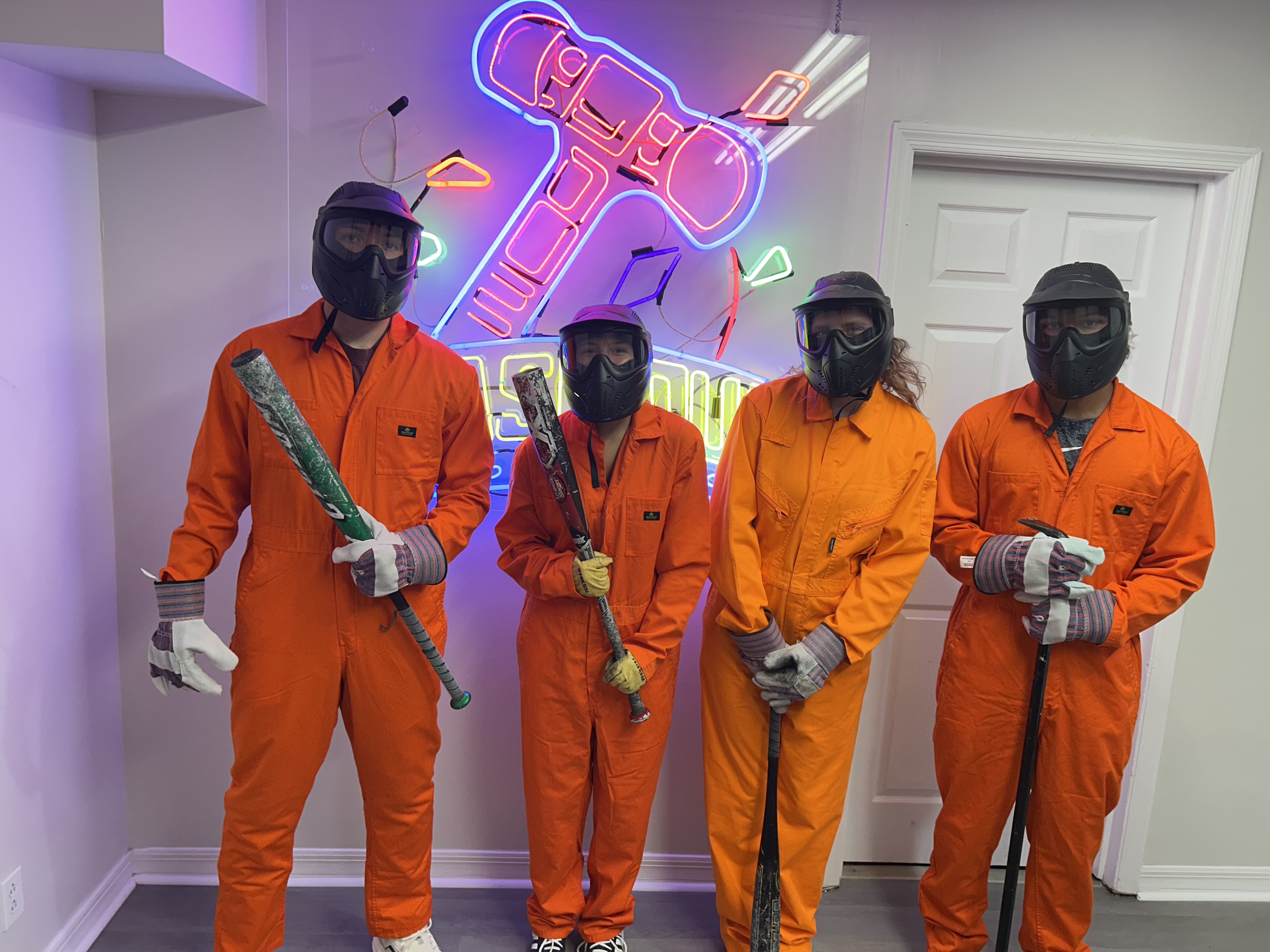 Crash Out Rage Rooms customers in orange jumpsuits and protective gear selecting bats from a bucket of smash tools