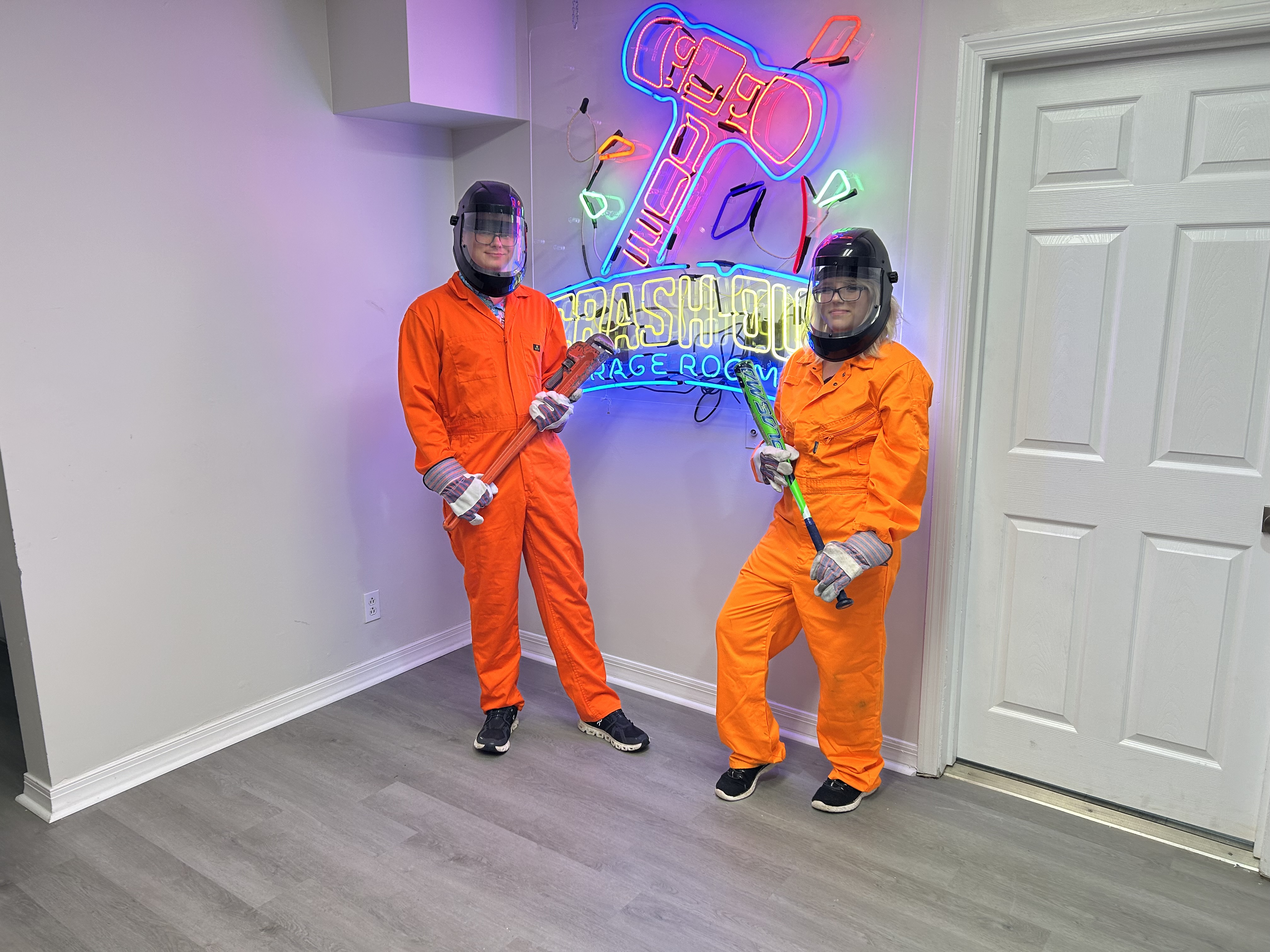 Large group of Crash Out customers in orange jumpsuits holding bats and smash tools in front of neon sign