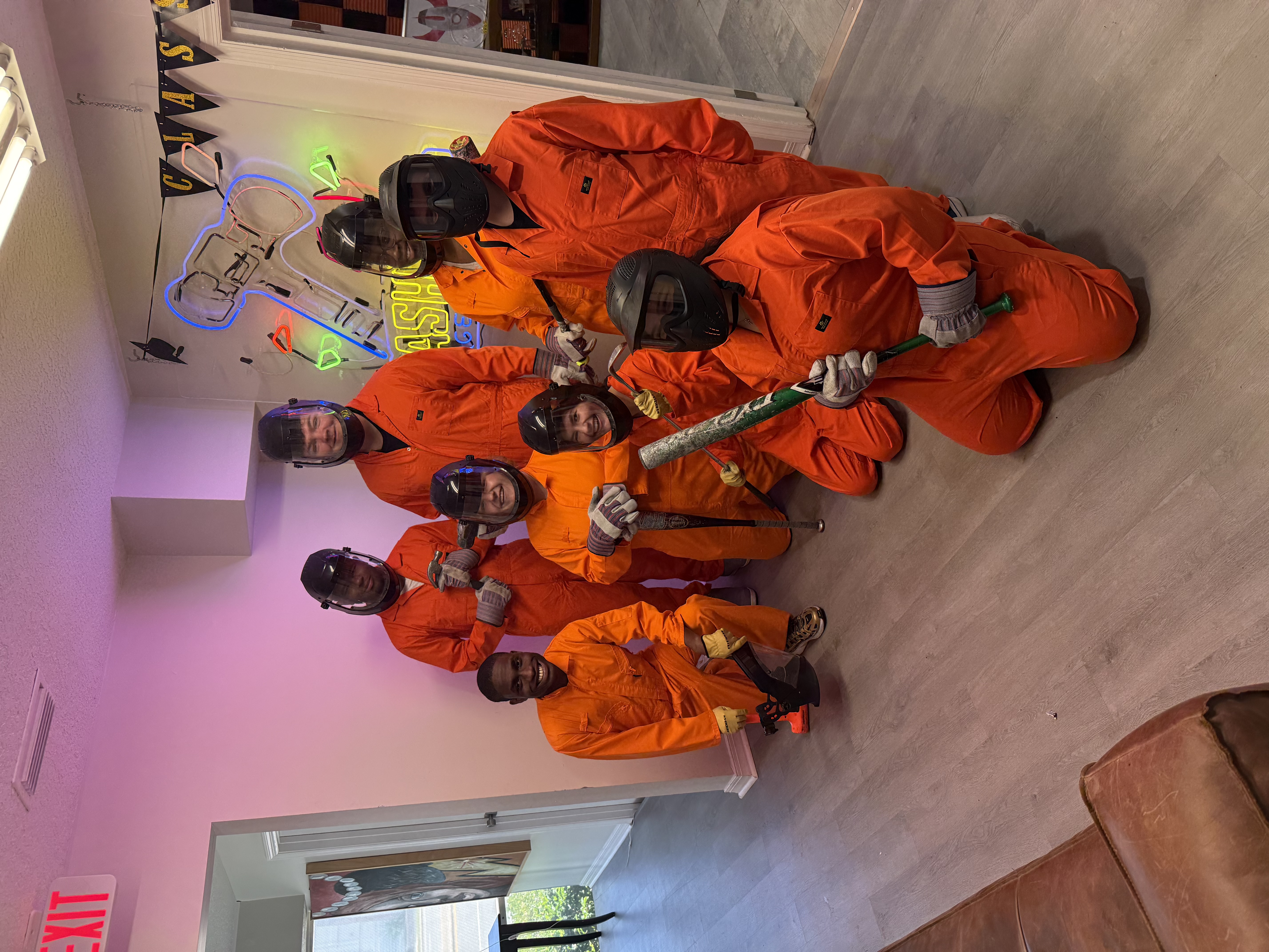 Group of eight Crash Out Rage Rooms guests in orange protective gear posing together