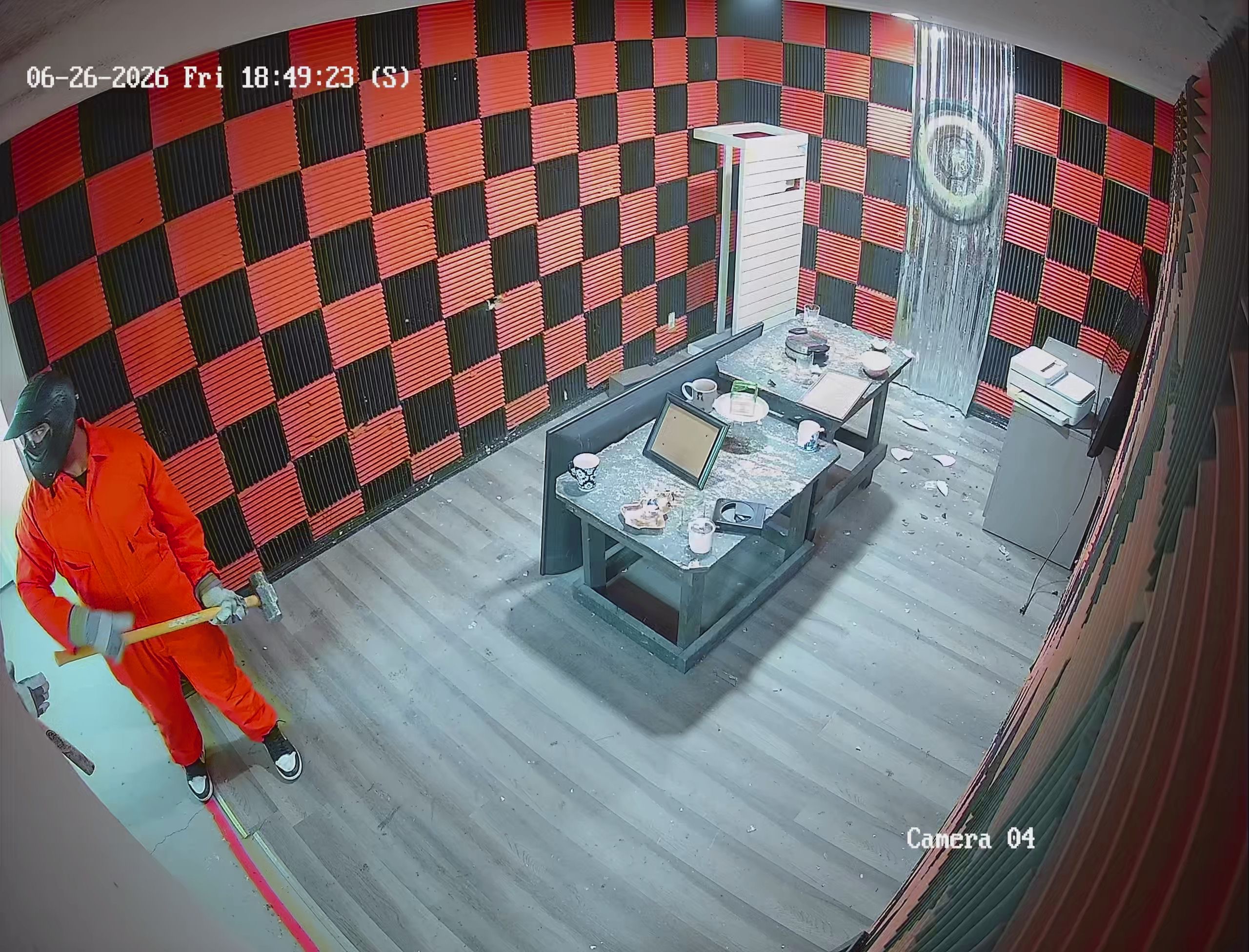 Security camera footage of Crash Out Rage Rooms customer in orange jumpsuit swinging sledgehammer inside red and black rage room in Florida